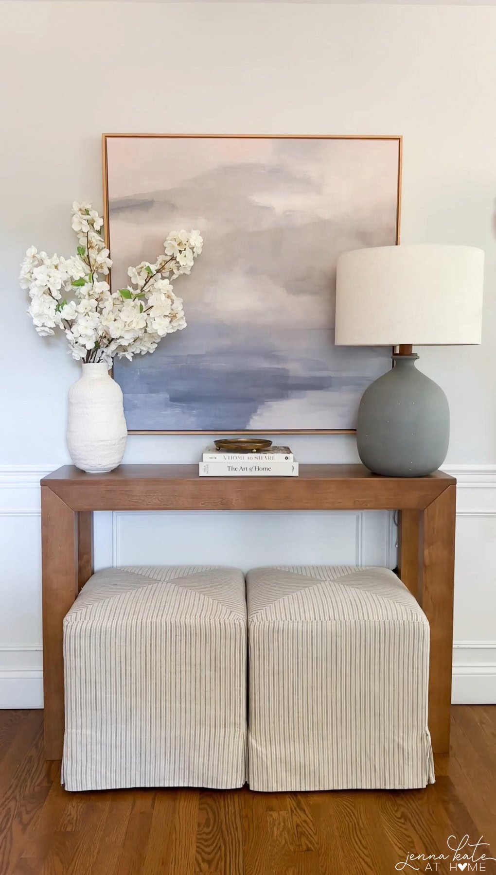 Narrow console table with matching ottomans and simple vase, styled for an entryway.