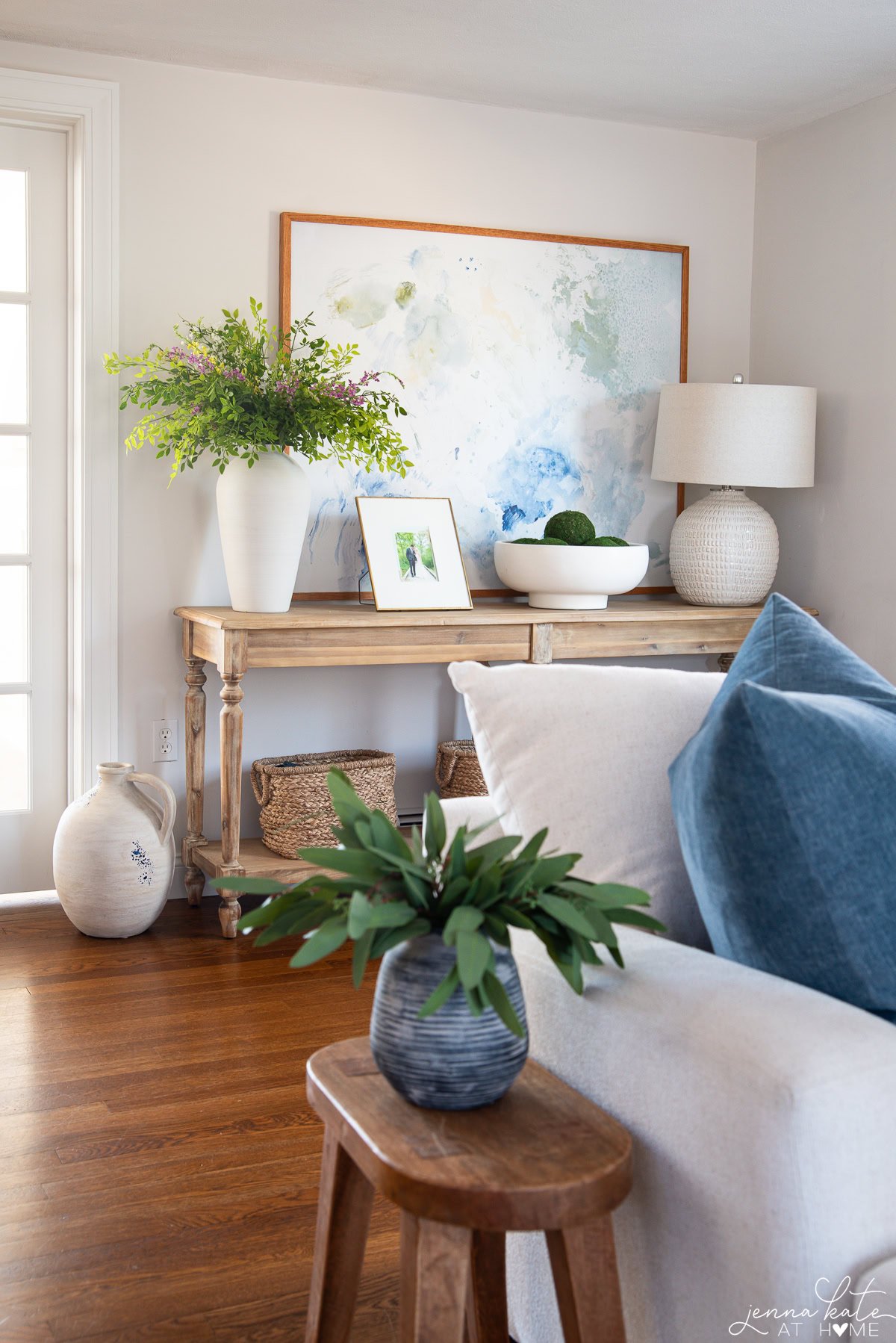 Neutral console table decor with tall vases, layered art, and organic textures in a living room.
