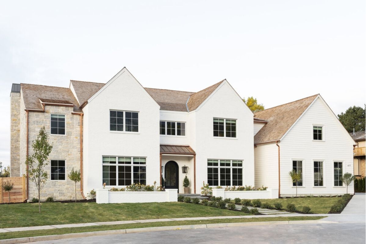 An exterior view of a large house painted a creamy off-white with brown accents.
