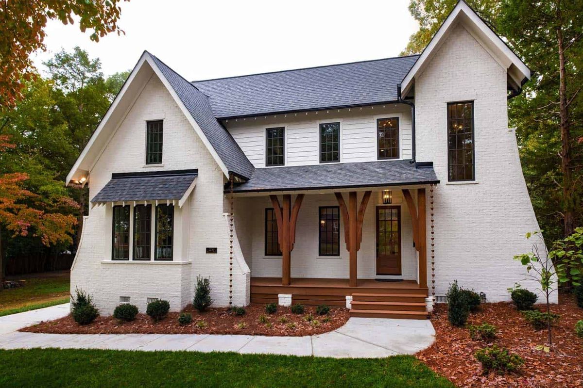 A classic white house with black shingled and brown beams accents on the front porch.