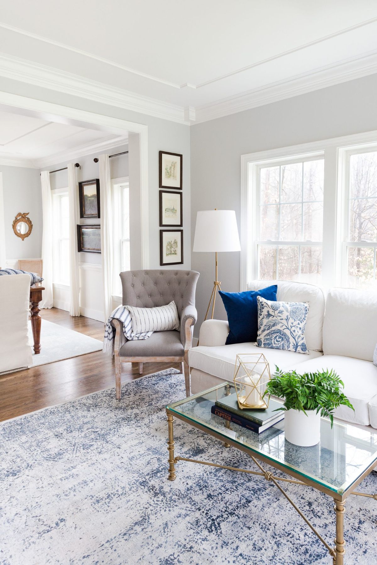 A family room painted in Passive with a cream couch and gold coffee table shown. A blue and white large floor rug is underneath the coffee table and there is a collection of frames hung on the wall.