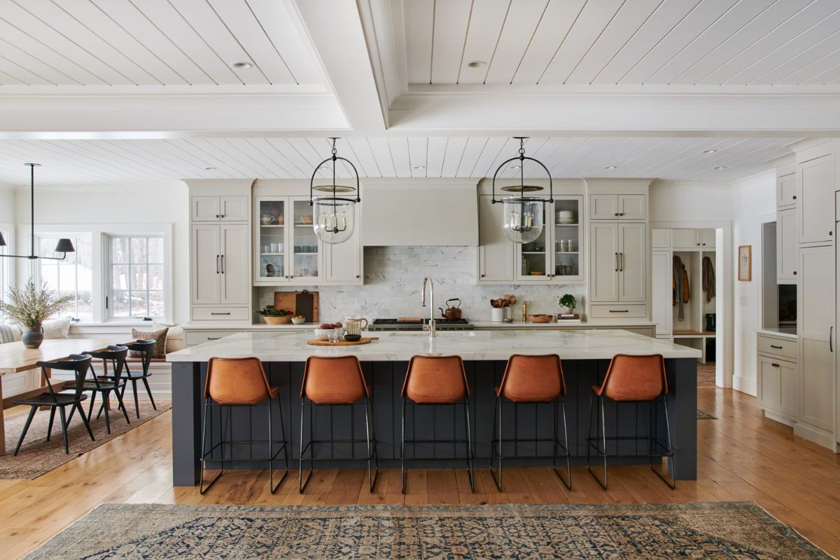 a large kitchen island painted wrought iron with white marble countertops and rustic leather counterstools.