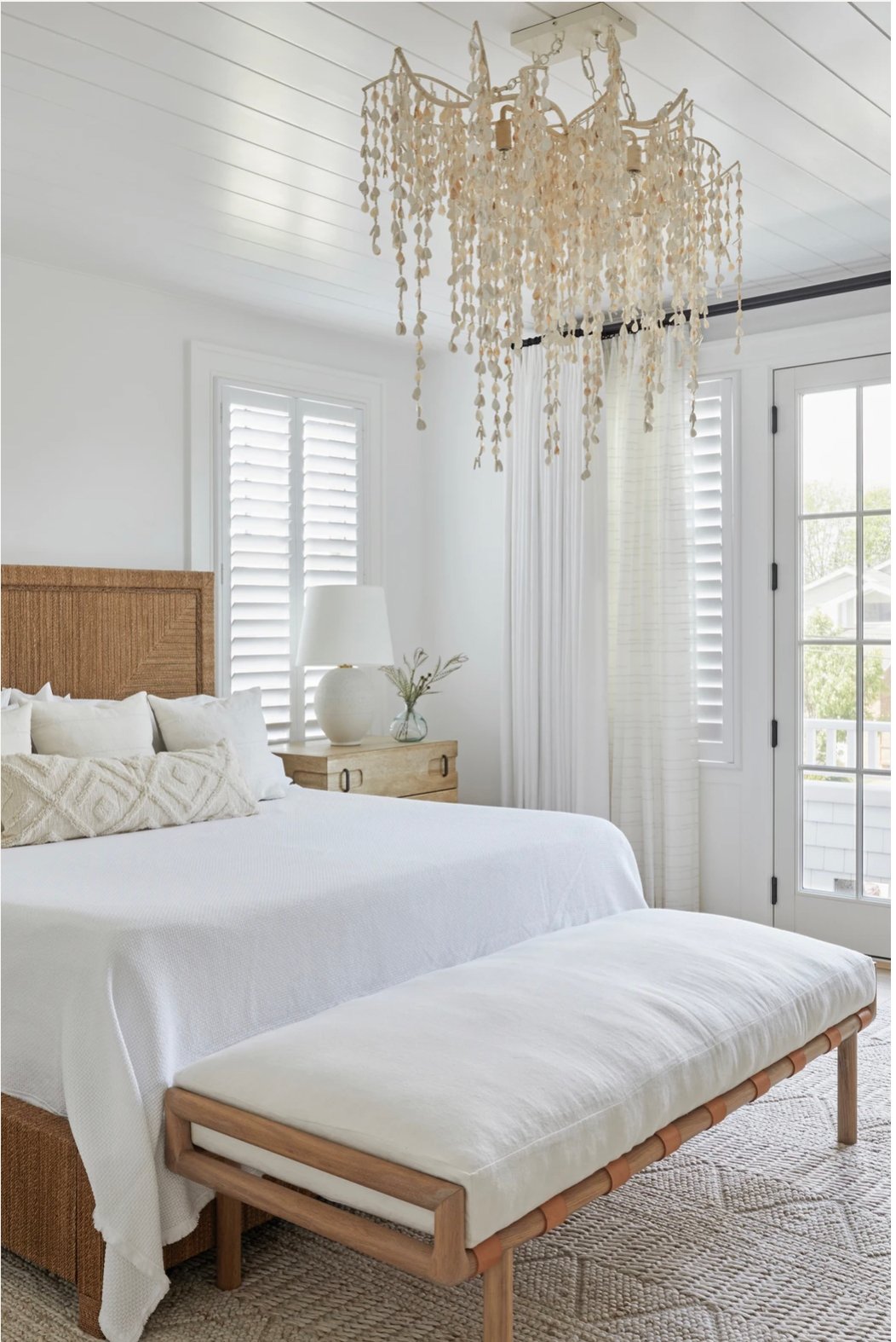 bedroom with white walls, woven bedframe and a dramatic chandelier.