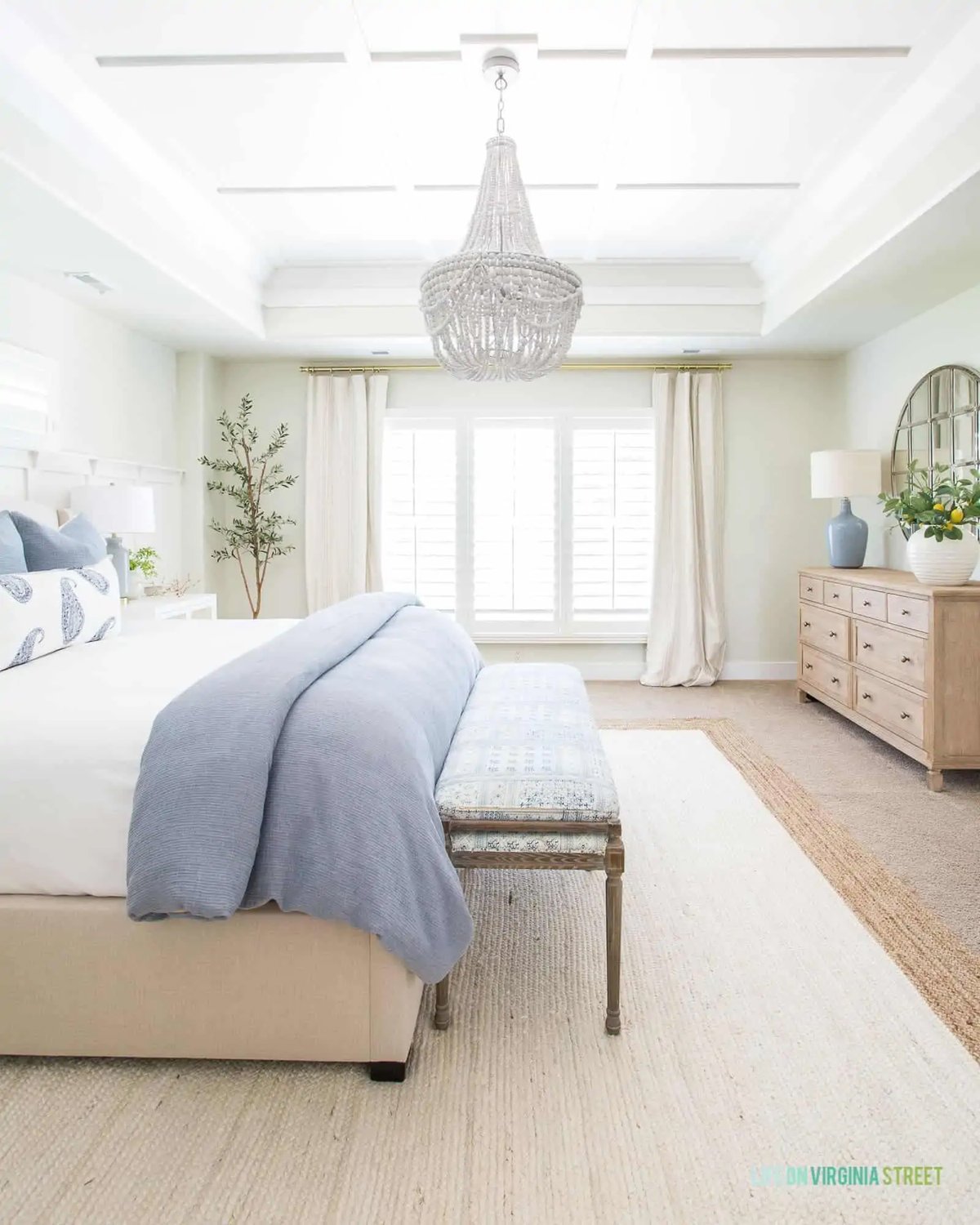 large bedroom with a beaded chandelier and white bedding with a blue quilt folded on the end.