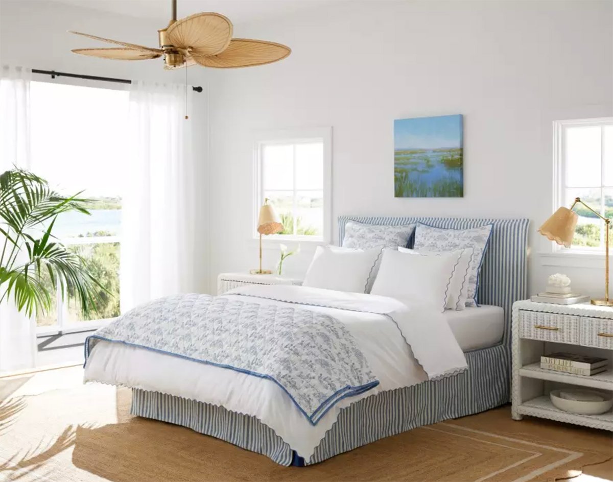 coastal bedroom with striped upholstered bed, white woven nightstands and blue and white bedding.