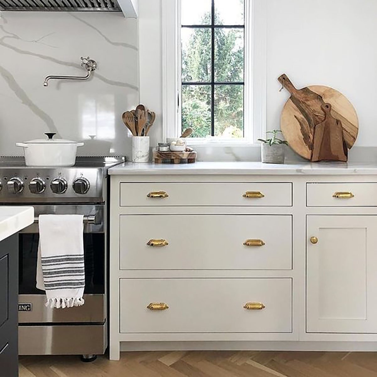 Benjamin Moore Classic Grey kitchen cabinets with gold hardware. Black trim windows paired with wood kitchen utensils and boards.