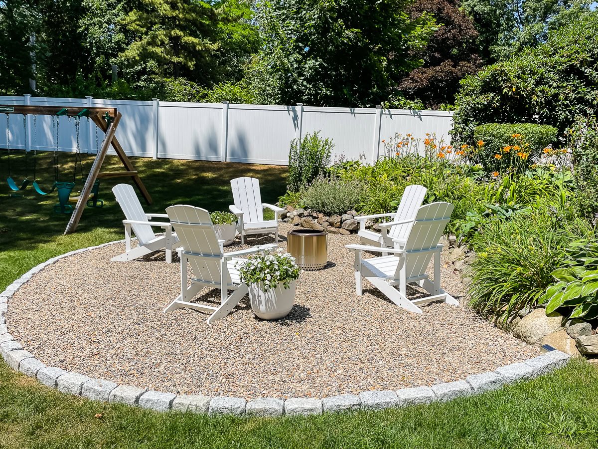 gravel firepit with white adirondack chairs and a solo stove.