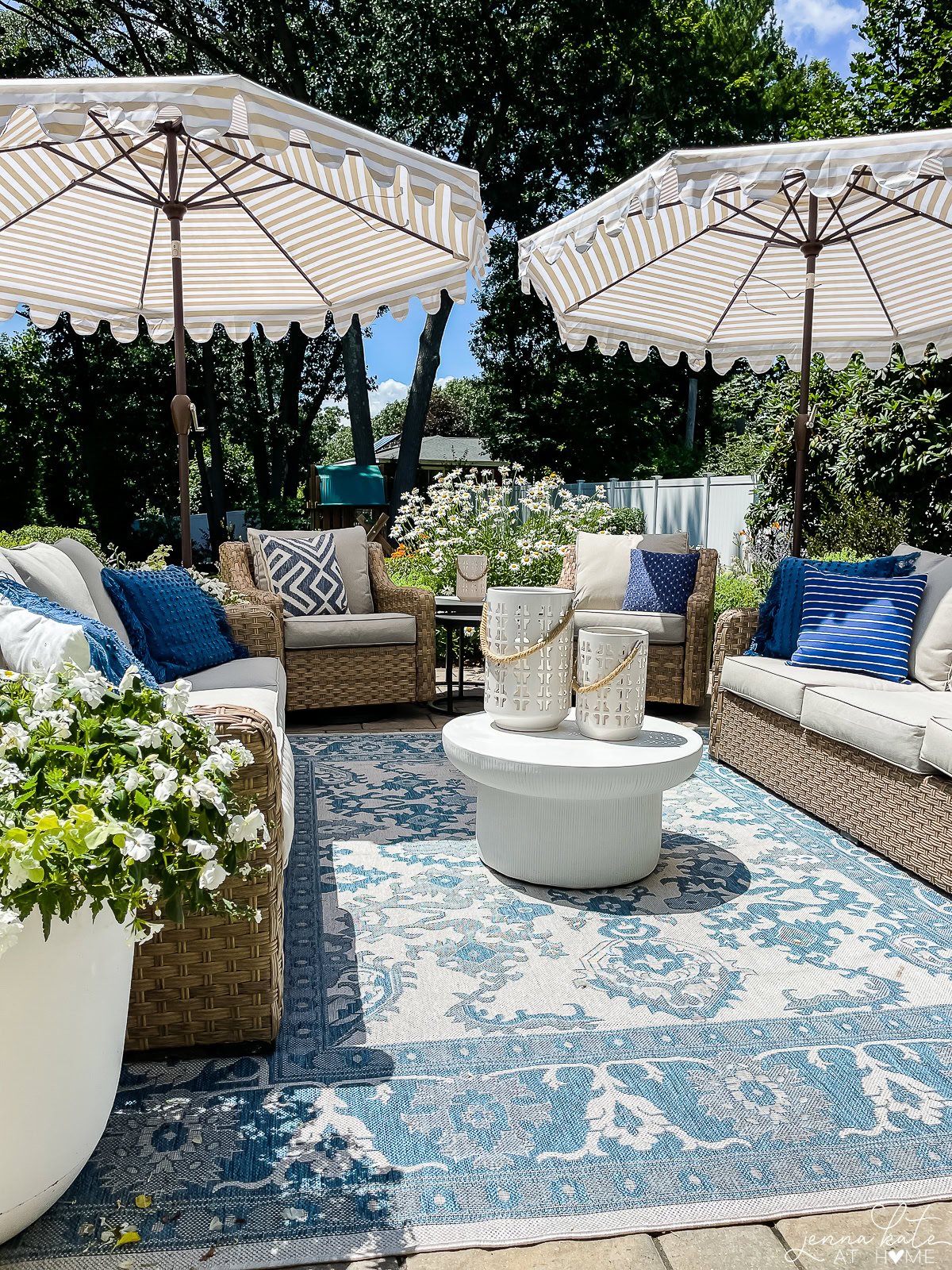 patio seating area with wicker furniture, an area rug and two large umbrellas.