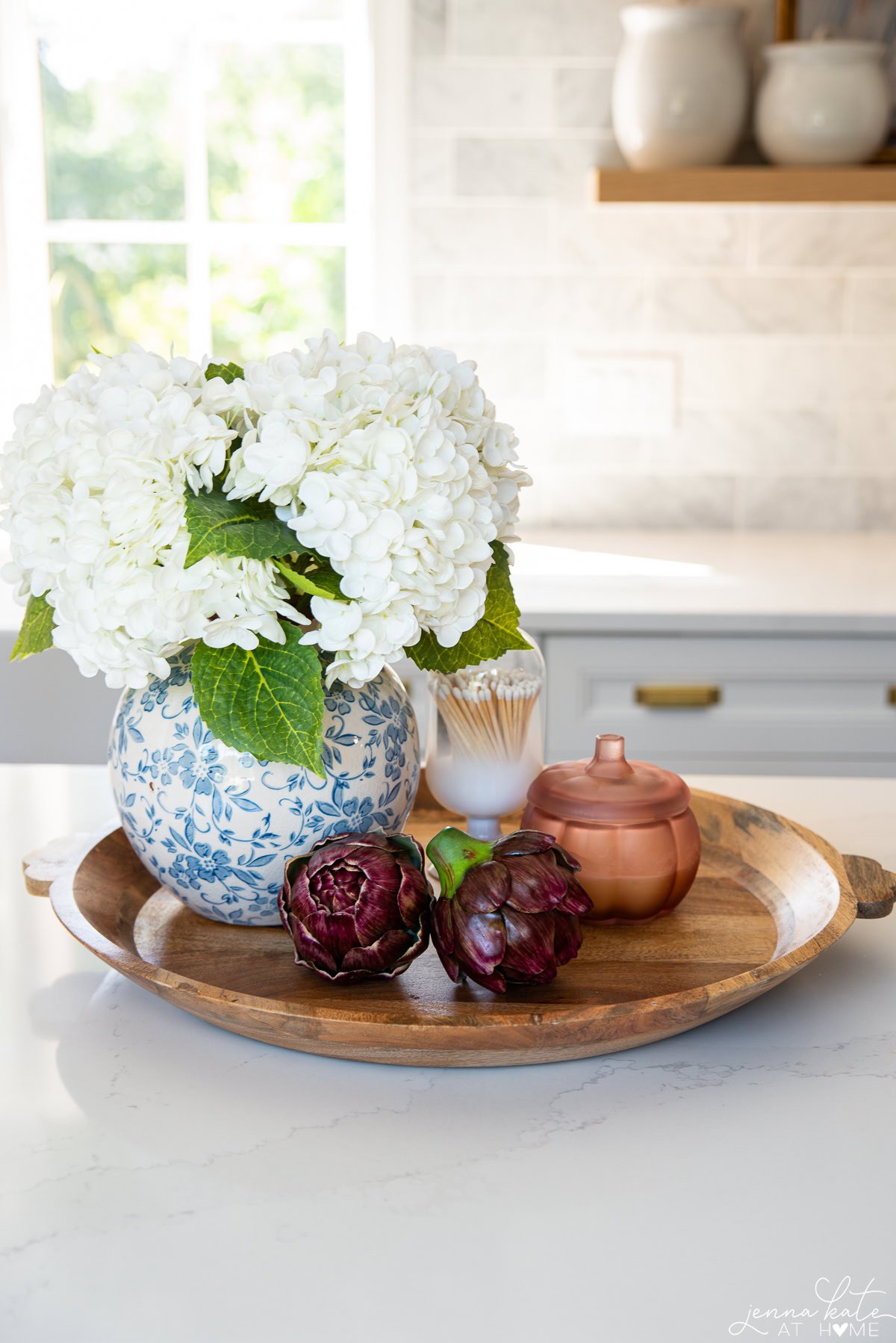 large round tray with a vase of flowers, faux artichokes, a candle and a cloche of matches.