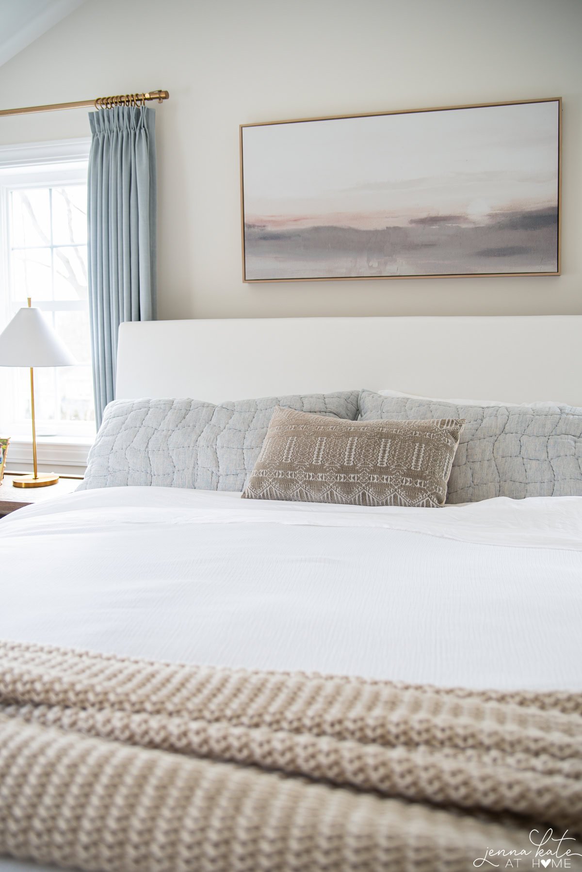 white bedding with blue shams and an accent lumbar pillow.