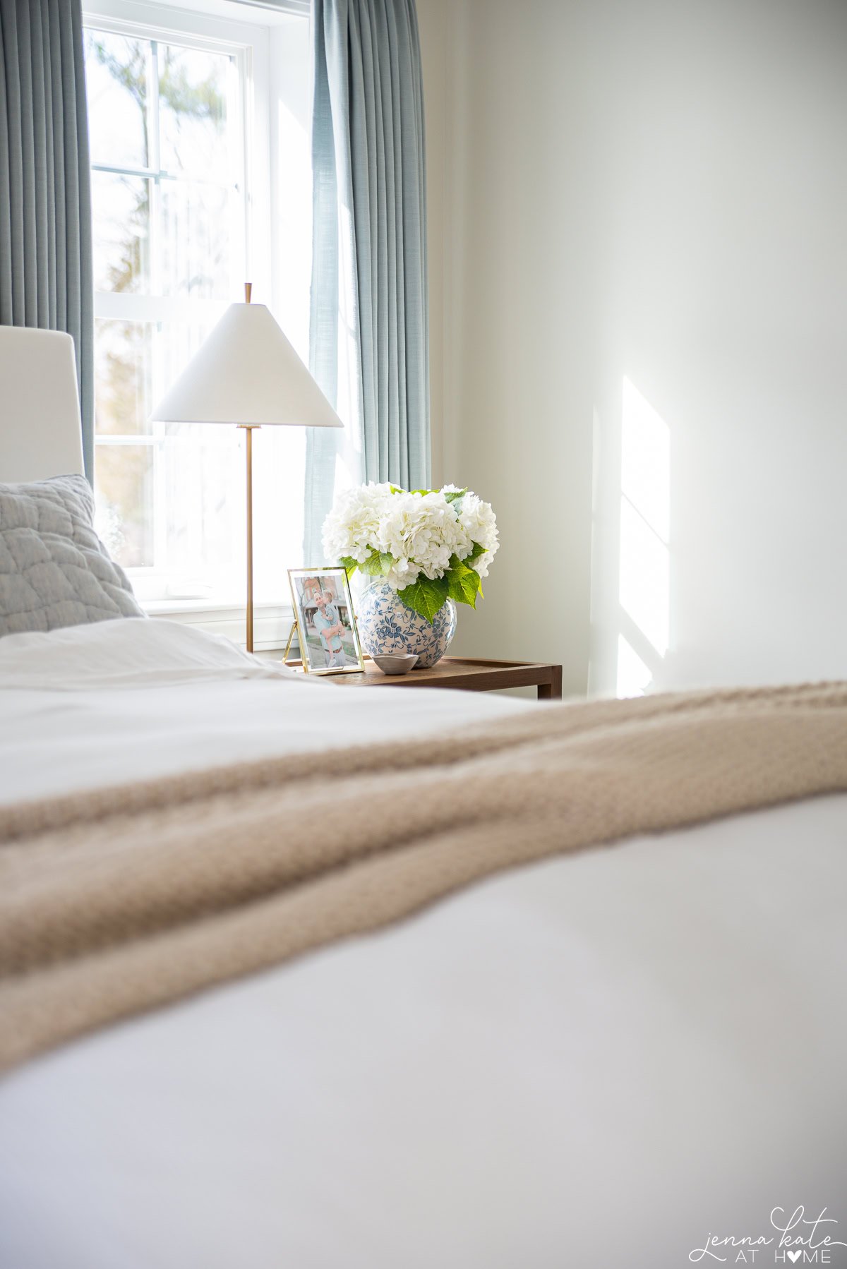 sleek lamp on nightstand with a vase of faux hydrangeas.