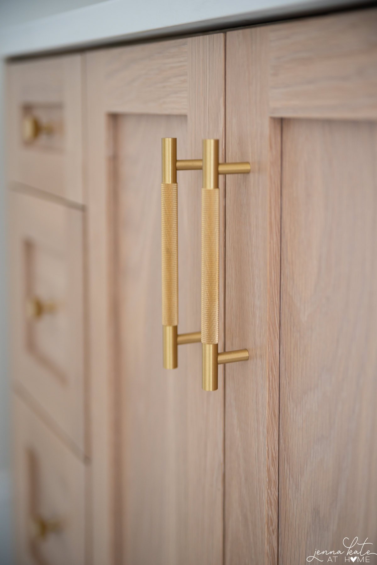 Brass drawer pulls on white oak vanity cabinet in warm modern bathroom.