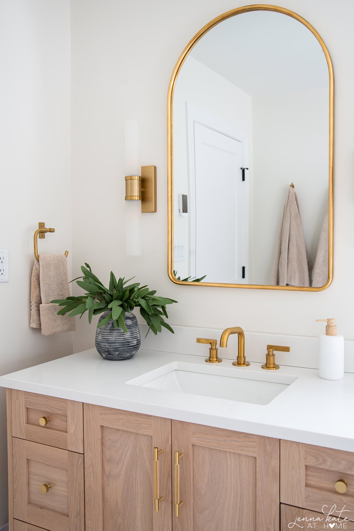 White oak vanity with brass fixtures, mirror and sconces and white quartz countertops.
