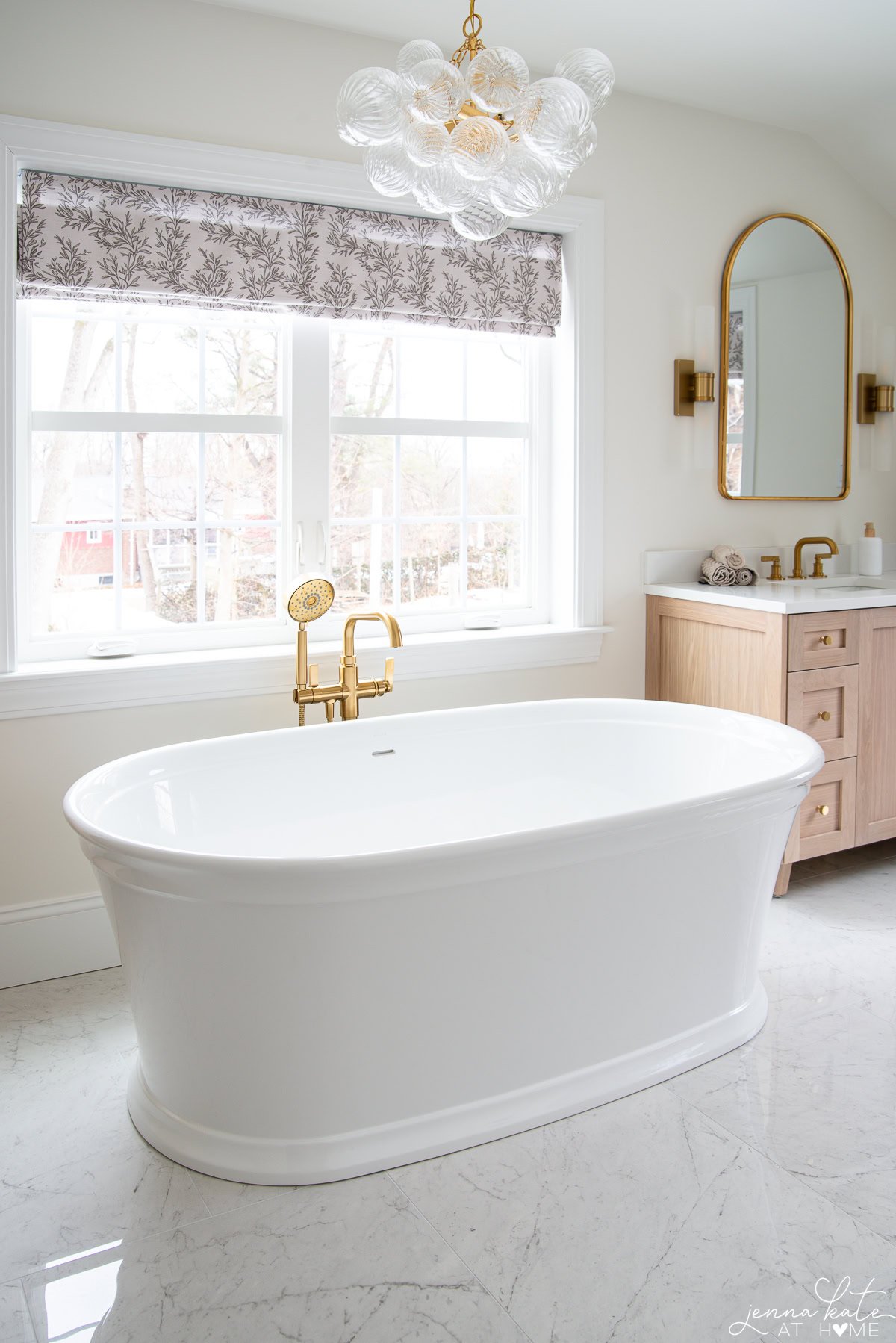 Freestanding Kohler soaking tub with bubble chandelier in bright modern bathroom.