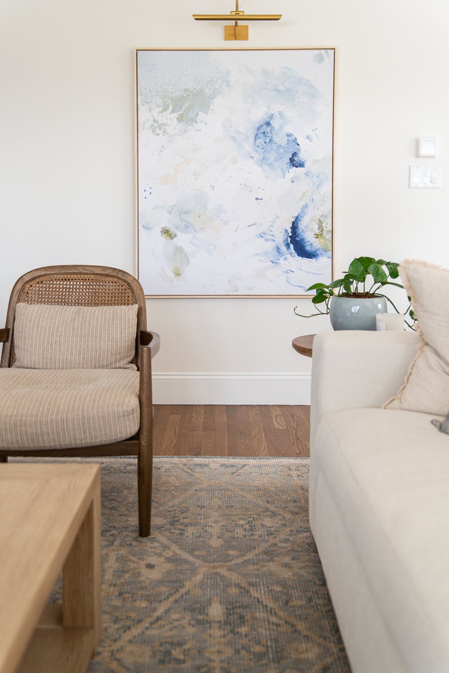 Large art on the family room wall with a brass library sconce over it.