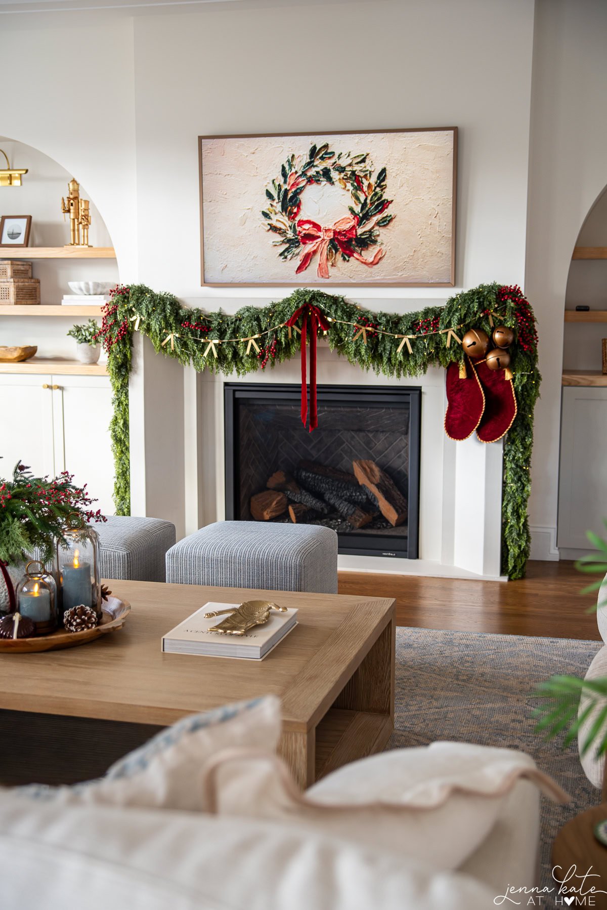 Garland hanging over the mantel with bows and red ribbon. There's a cluster of bells in the corner and two red stockings.
